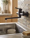 Blutide black wall-mounted kitchen sink mixer against a stone splashback