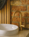 Blutide brushed brass basin mixer against an exposed brick wall