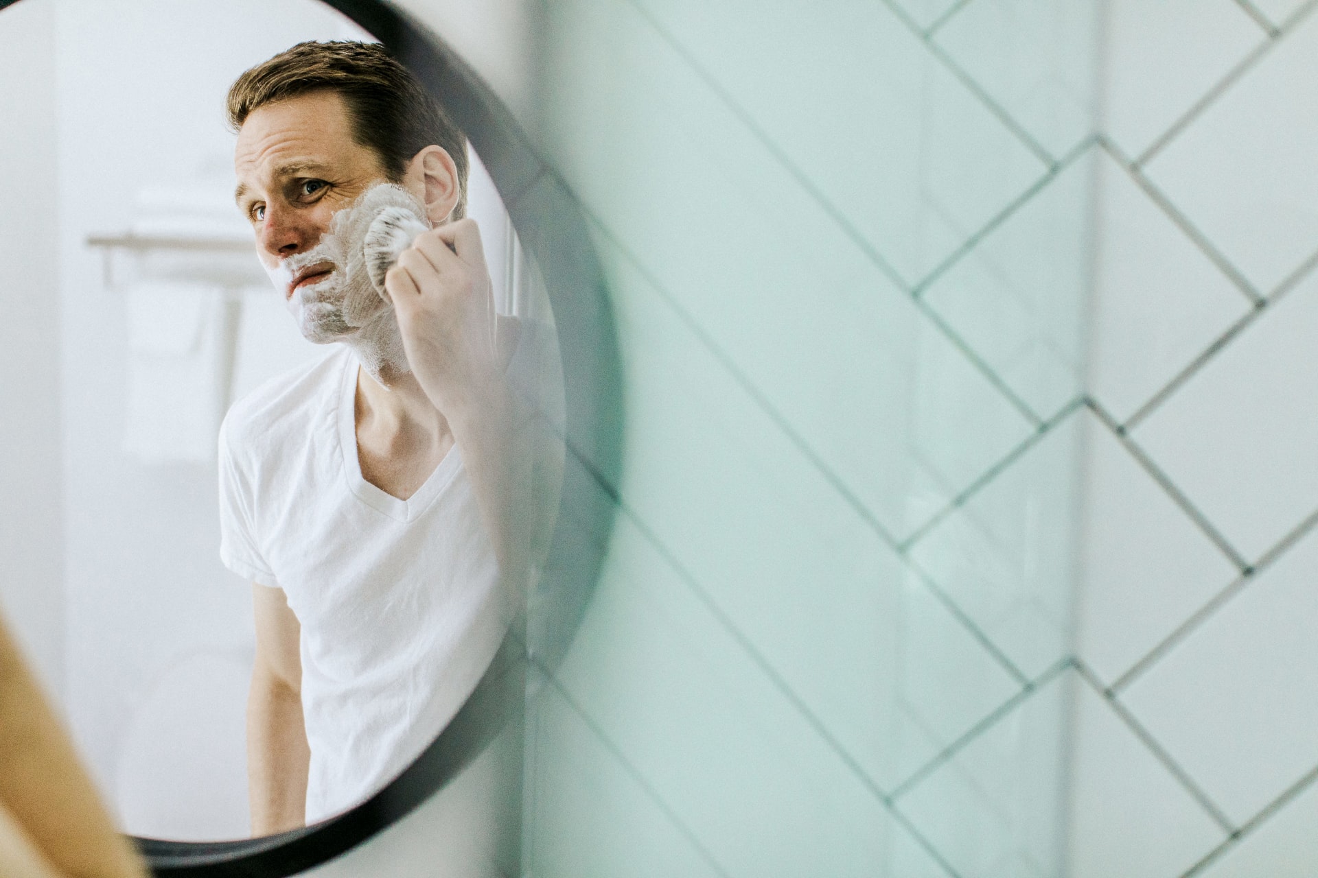 A man shaving while using a well lit bathroom mirror